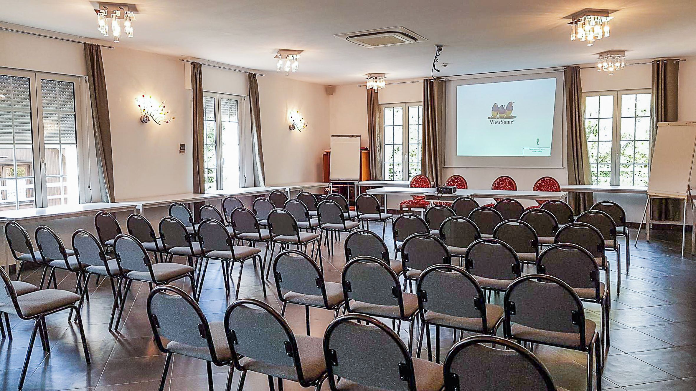Een vergaderzaal met rijen stoelen, een scherm voor een beamer en een whiteboard.