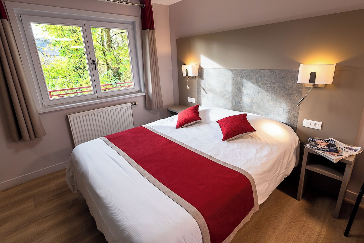 Et hotelværelse med en seng, to sengeborde med lamper, et vindue med gardiner og en radiator.