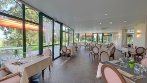 A restaurant with large windows, outdoor seating, and a tiled floor. - Hotel La Sapiniere (Hallines)