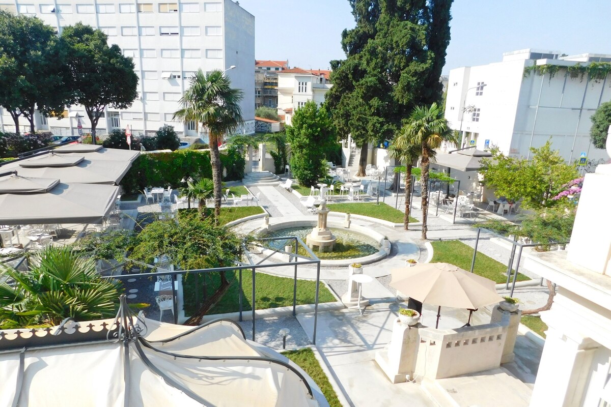 Eine Dachterrasse mit Sitzgelegenheiten im Freien, einer zentralen Fontäne und umgebender Bepflanzung.