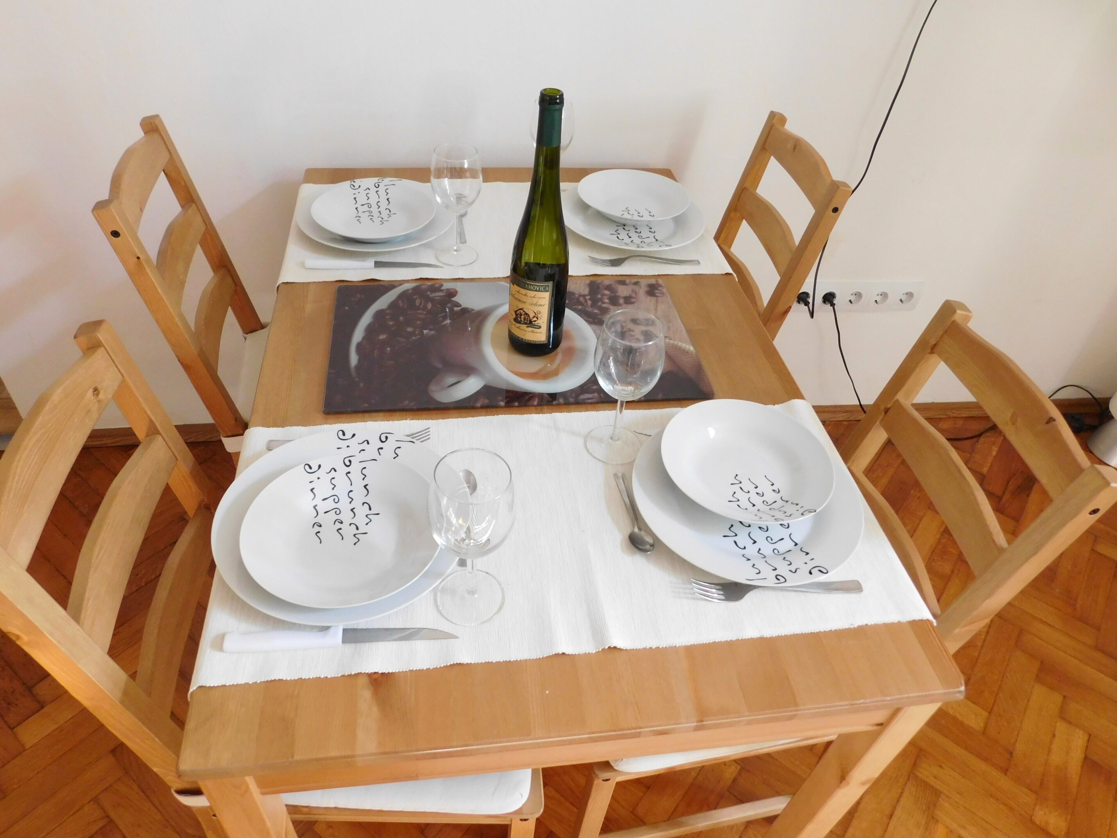 Ein Holztisch mit vier Stühlen, einer Weinflasche und Tellern mit handgeschriebenen Notizen.