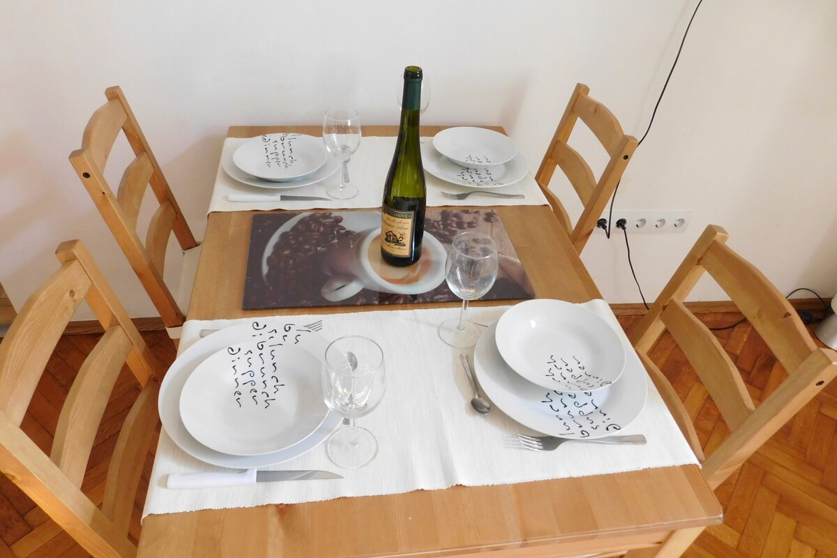Ein Holztisch mit vier Stühlen, einer Weinflasche und Tellern mit handgeschriebenen Notizen.