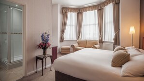 A hotel room with a large bed, two armchairs, a small table with a vase of flowers, and a window with curtains. - The Devonshire Park Hotel (Eastbourne)