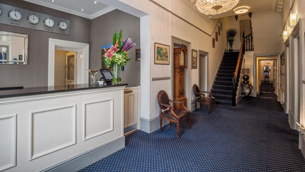A reception area with a counter, chairs, a chandelier, clocks, and a staircase. - The Devonshire Park Hotel (Eastbourne)