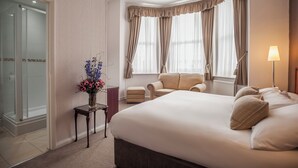 A hotel room with a large bed, two armchairs, a small table with a vase of flowers, and a window with curtains. - The Devonshire Park Hotel (Eastbourne)