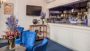A bar area with a television mounted on the wall, a bar stocked with various bottles, and blue chairs. - The Devonshire Park Hotel (Eastbourne)