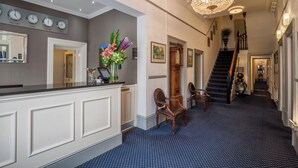 A reception area with a counter, chairs, a chandelier, clocks, and a staircase. - The Devonshire Park Hotel (Eastbourne)