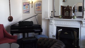 A living room with a grand piano, a red armchair, a tufted sofa, a small round table, and a fireplace with a mirror above it. - The Devonshire Park Hotel (Eastbourne)