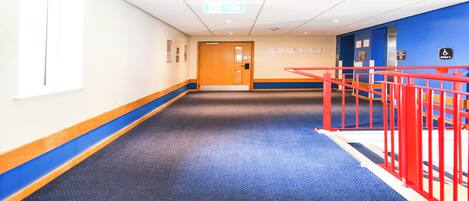 A hallway with a blue carpet, a wooden door, and a red railing.