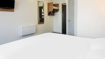 Un dormitorio con una cama, un televisor montado, un espejo, un perchero y una puerta.