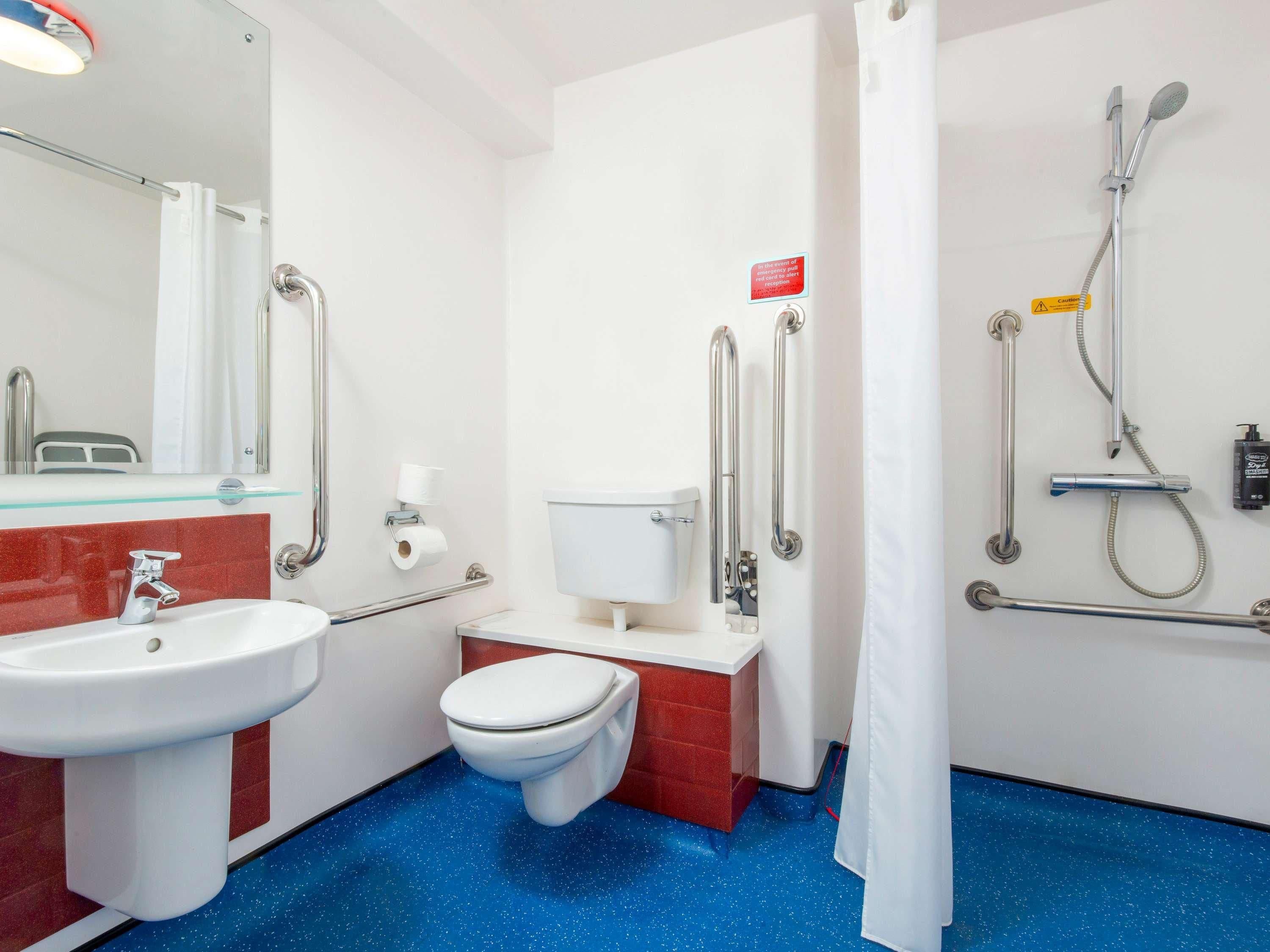 A bathroom with a sink, toilet, and shower area, equipped with handrails and a shower head.