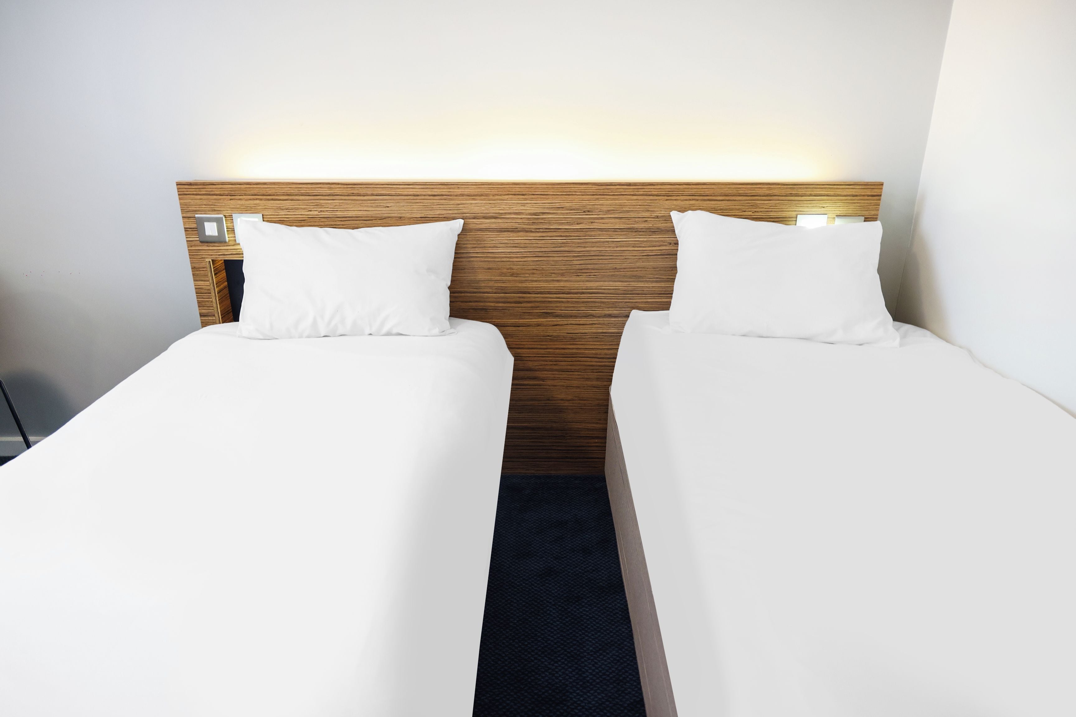 A hotel room with two single beds, a wooden headboard, and a nightstand with a lamp.