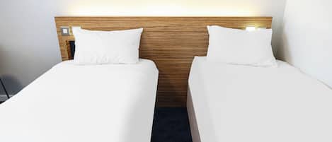 A hotel room with two single beds, a wooden headboard, and a nightstand with a lamp.