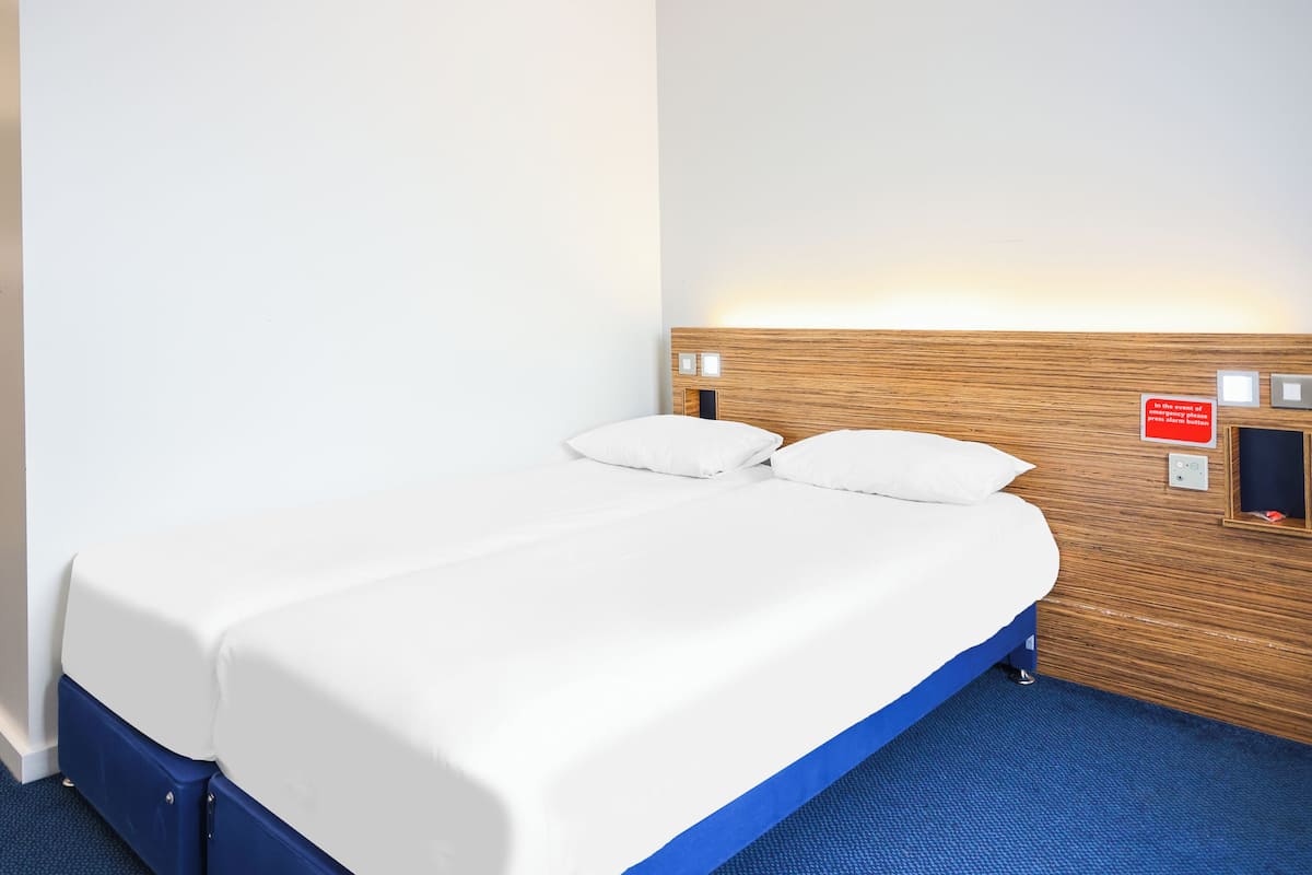 A single bed with a wooden headboard, white bedding, and a blue carpeted floor.