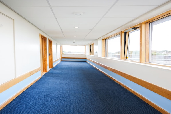 A long, narrow corridor with blue carpet, wooden trim, and large windows on one side.