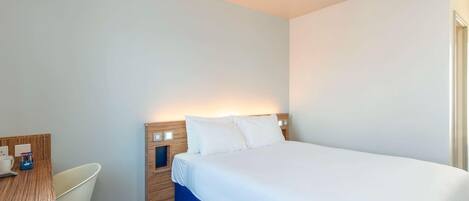 A hotel room with a bed, a desk, a chair, and a nightstand.
