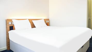 A neatly made bed with white linens, a wooden headboard, and bedside lamps.