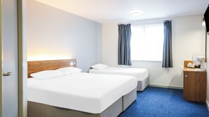 A hotel room with two beds, a window with curtains, a bedside table with a lamp, and a small wooden cabinet. - Ibis Budget Lancaster Centre (Lancaster)