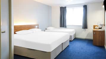 A hotel room with two beds, a window with curtains, a bedside table with a lamp, and a small wooden cabinet.