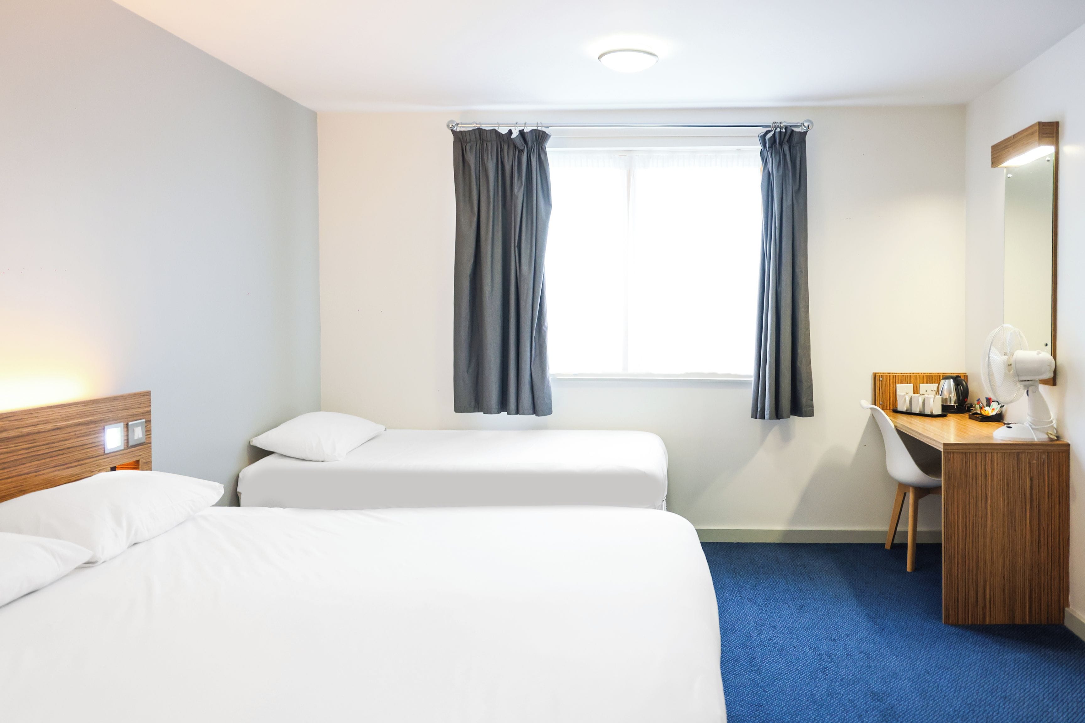 Habitación de hotel con dos camas, un escritorio, una silla, un espejo y una ventana con cortinas.