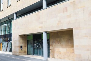 A modern building facade with a stone exterior, large glass entrance doors, and a visible security keypad.