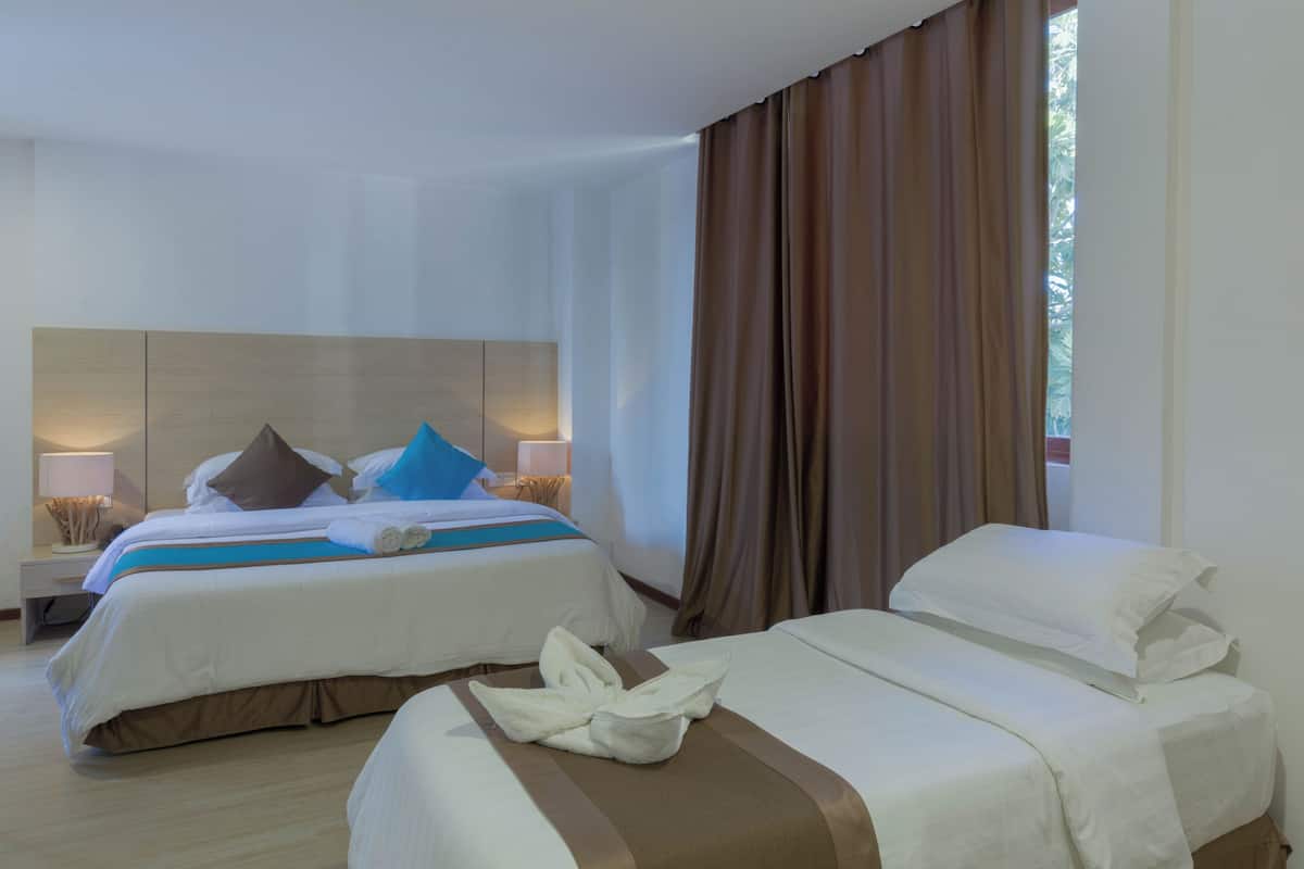 Habitación de hotel con dos camas, una mesita de noche con lámpara y vistas al exterior.