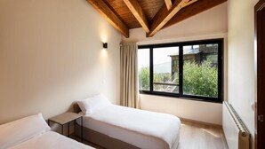 Un dormitorio con dos camas, techo de madera, ventana con vistas y un radiador.