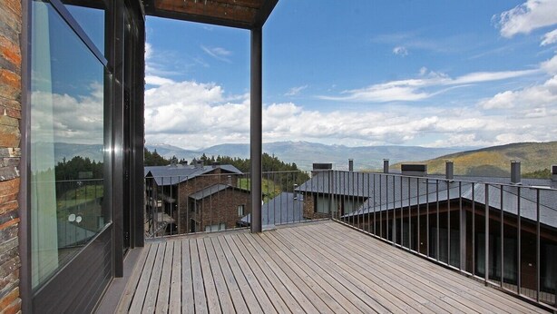 Terraza de madera con paredes de vidrio y vistas a un paisaje montañoso.