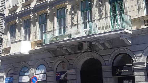 A multi-story building with a balcony, a shop sign, and parked cars. - Theaterland Classic Apartments (Budapest)