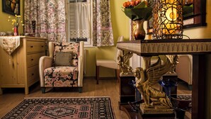 A cozy room with a floral-patterned armchair, a wooden cabinet, a patterned rug, and decorative items including a vase with flowers and a golden statue. - Theaterland Classic Apartments (Budapest)
