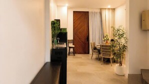 Un intérieur moderne avec un long couloir, un coin repas comprenant une table et des chaises, et une porte en bois.