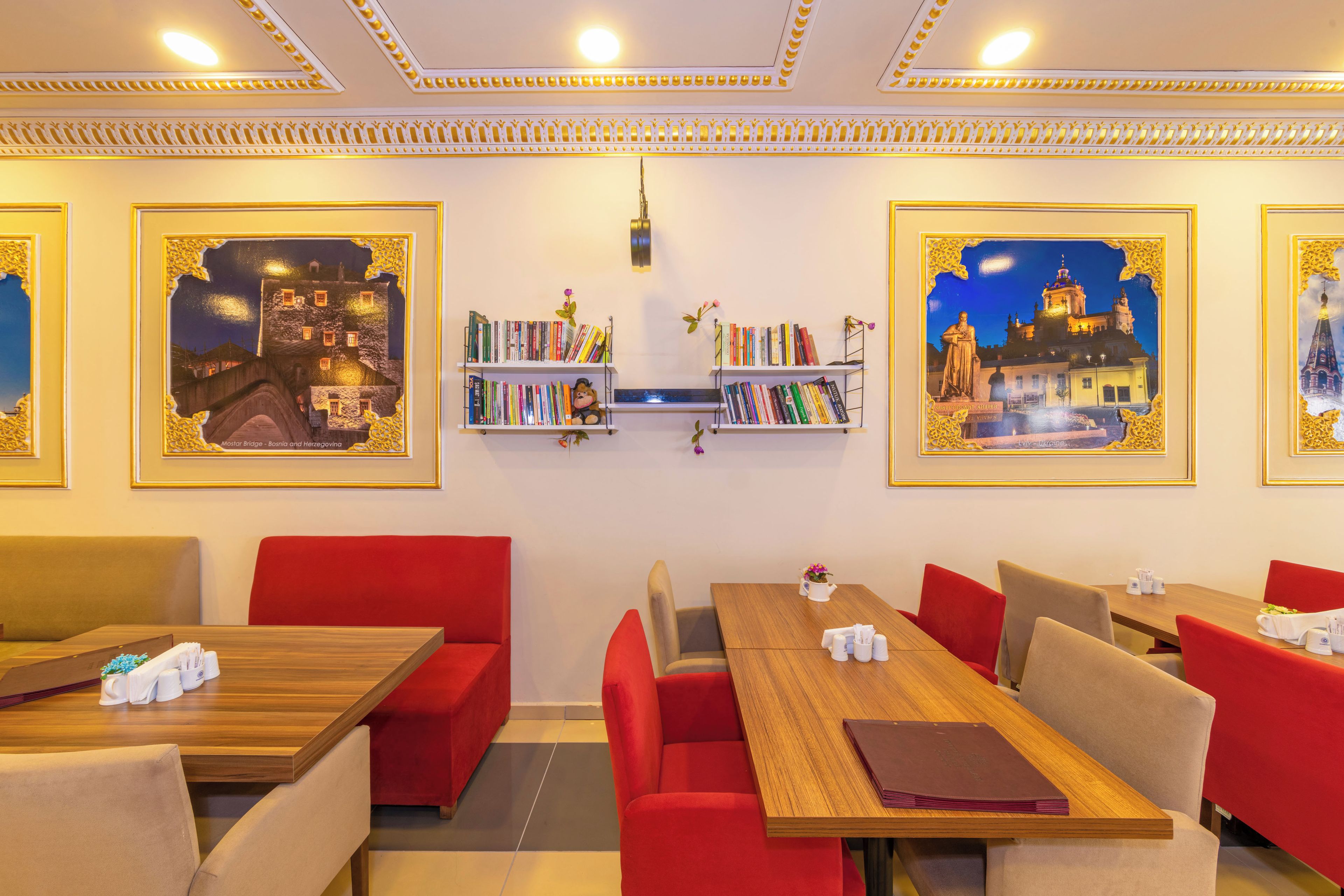 A hotel room with a wooden dining table, red upholstered chairs, a bookshelf with books, and framed pictures on the wall.