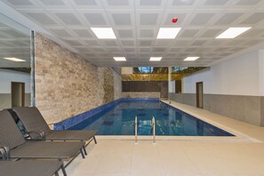 Una piscina interna con pavimento piastrellato, parete in mattoni e poltrone da relax.
