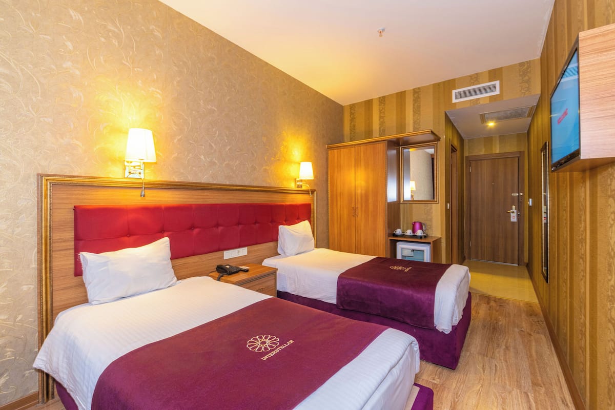 Habitación de hotel con dos camas, televisión, espejo y una mesita de noche con lámpara.