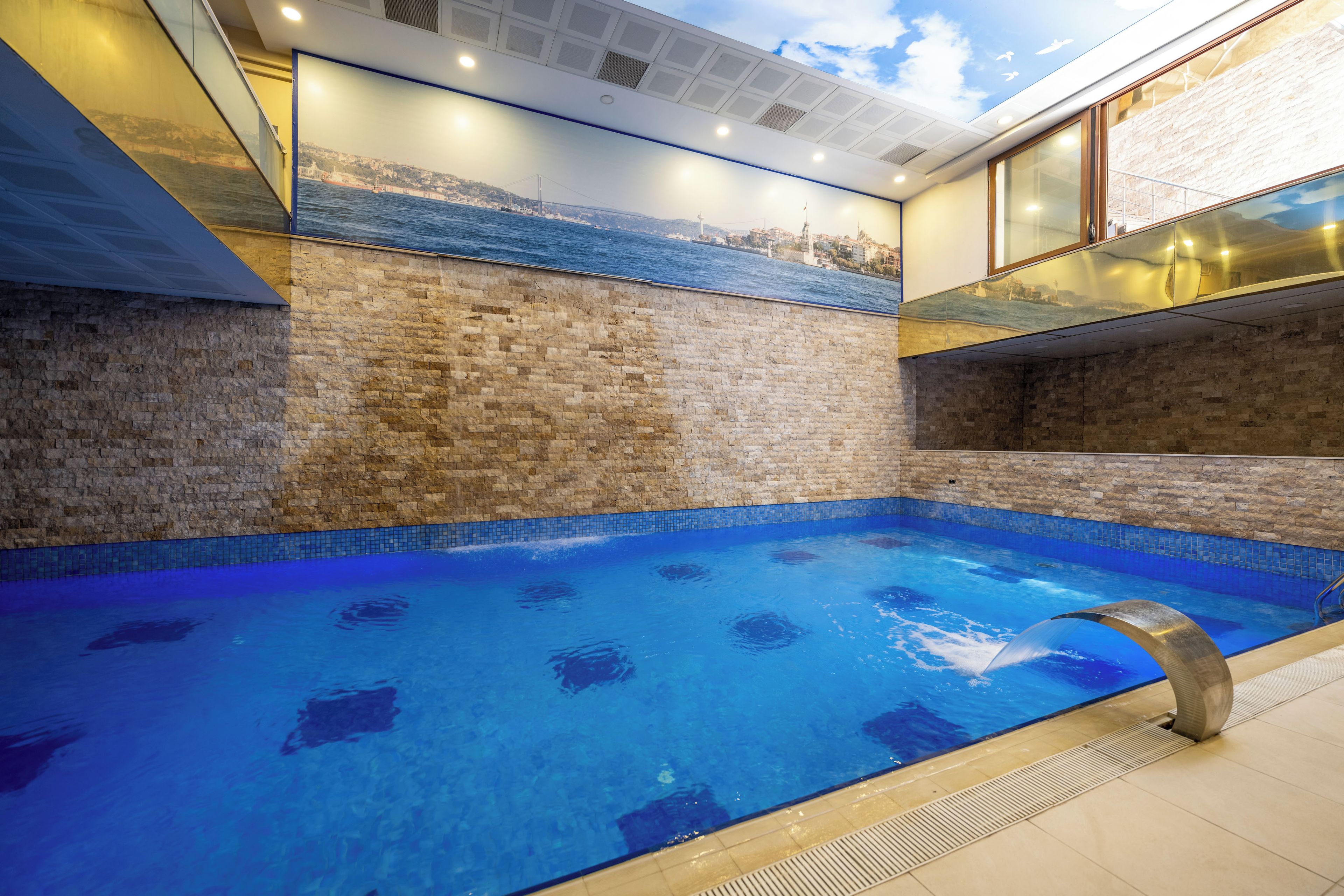 Una piscina con pared de vidrio y un mural de paisaje costero.