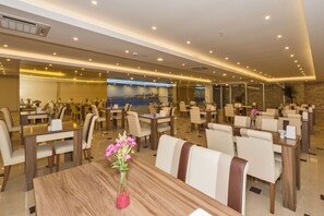 A hotel dining area with multiple tables and chairs, a large wall-mounted screen, and a modern ceiling design. - Harmony Hotel (Istanbul)