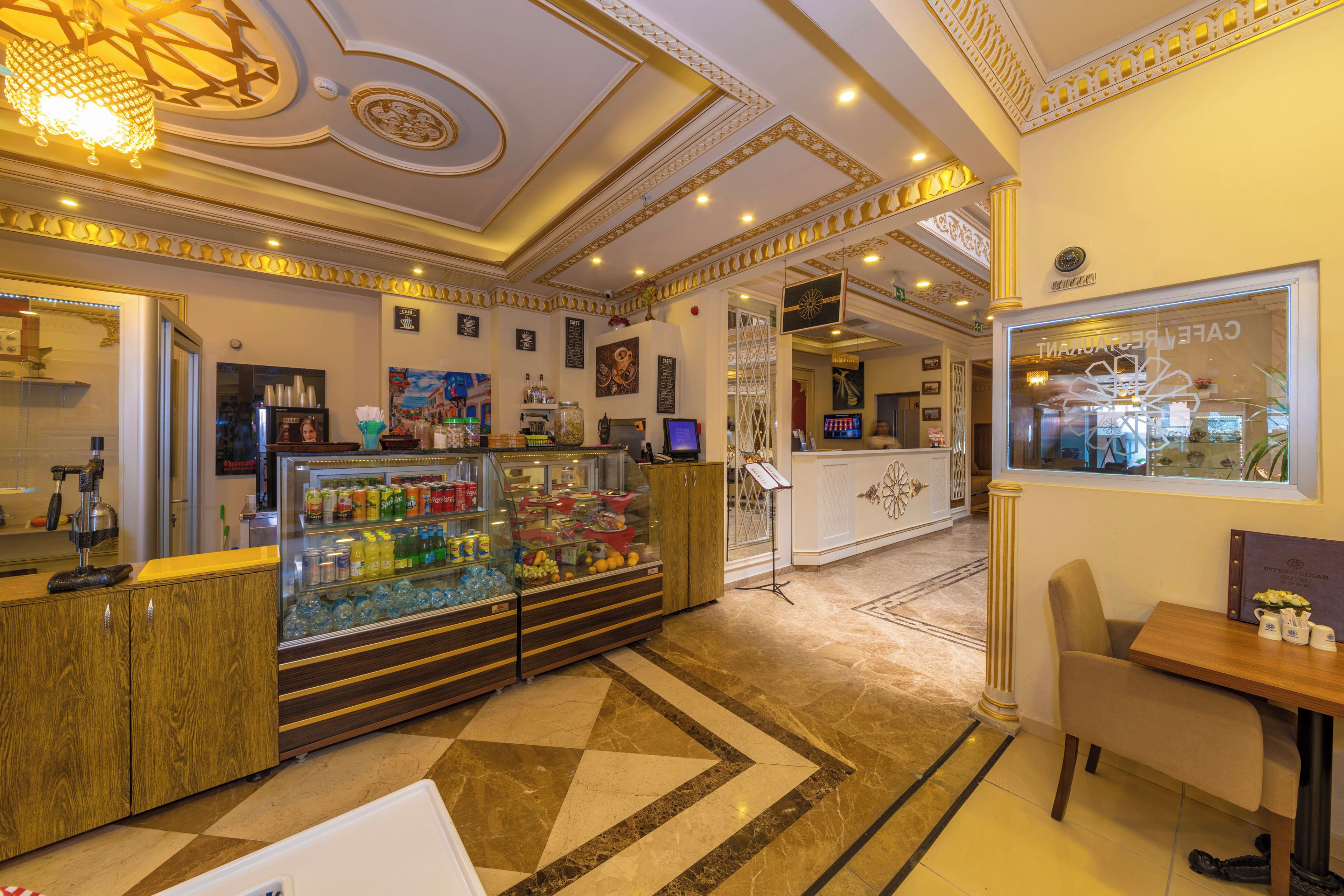 A hotel lobby with a reception desk, a glass display case with snacks, a seating area, and a decorative ceiling.