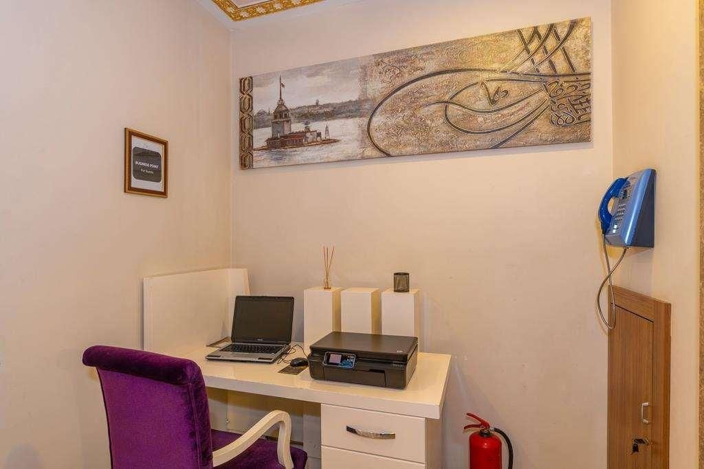 A room with a desk, a laptop, a printer, a purple chair, a wall-mounted telephone, and a fire extinguisher.
