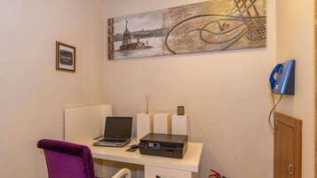 A room with a desk, a laptop, a printer, a purple chair, a wall-mounted telephone, and a fire extinguisher.