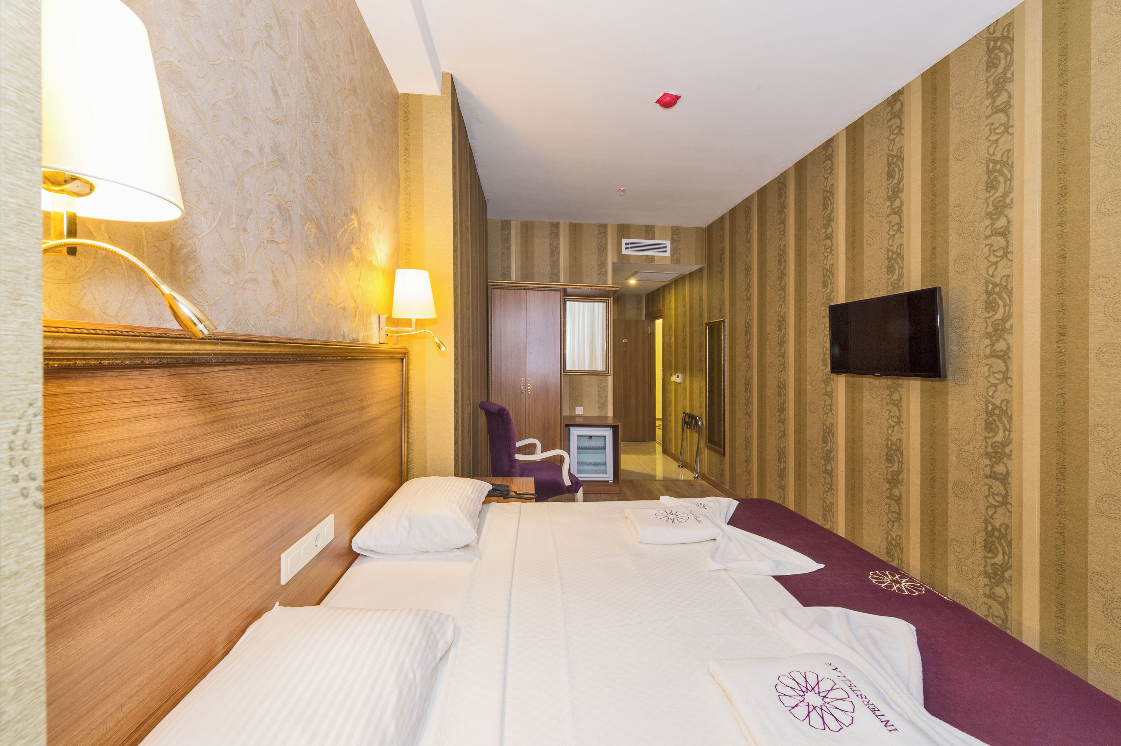 A hotel room with a bed, bedside lamps, a television, and a mirror.