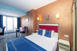 Una habitación de hotel con una cama grande, un escritorio, una silla, una mesita de noche y una lámpara de pared.