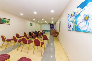 Una sala conferenze con un tavolo grande e sedie, uno schermo per proiettore e un quadro con fiori al muro.