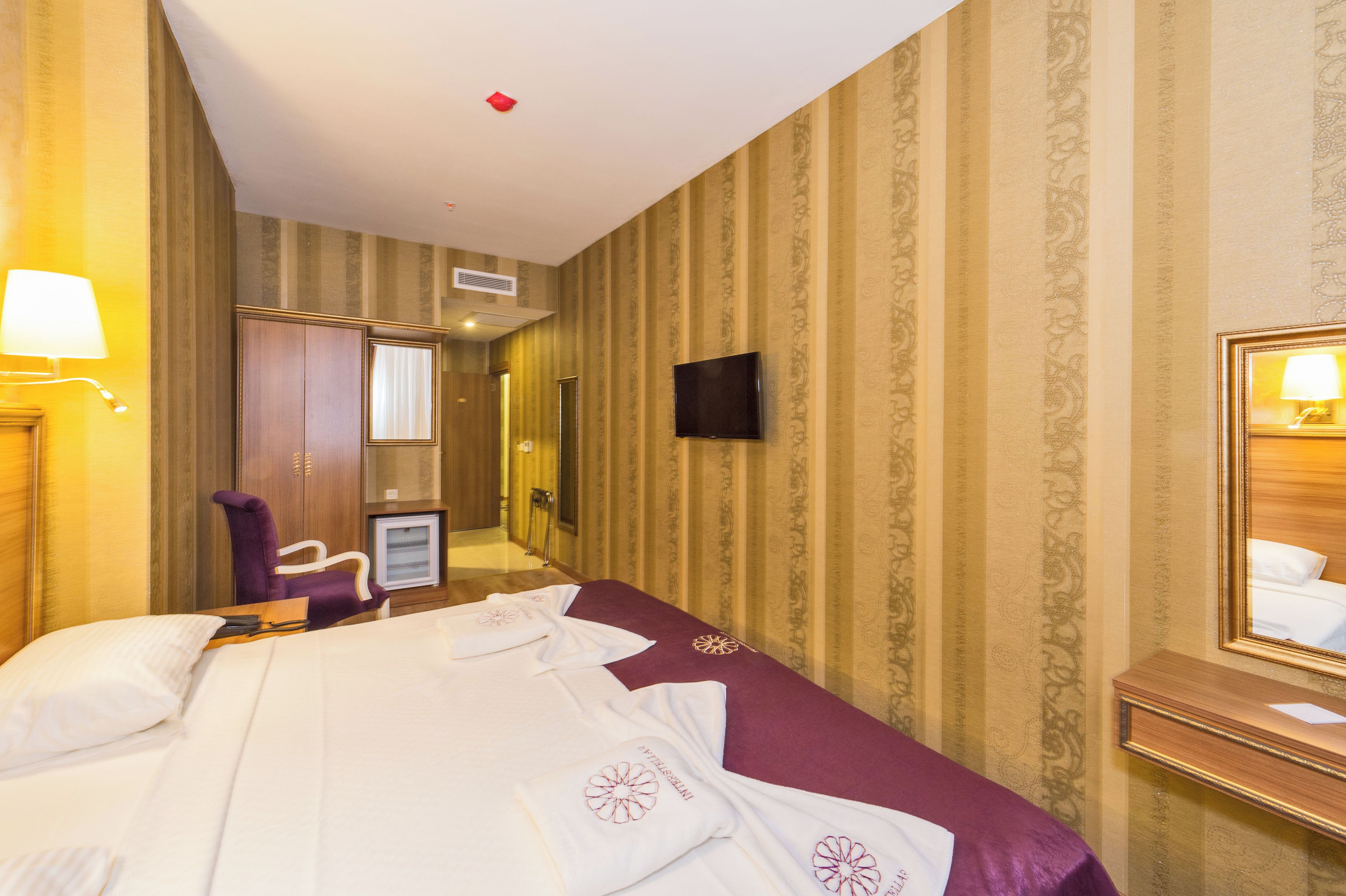 Ein Hotelzimmer mit Bett, Stuhl, Fernseher, Spiegel und Schreibtisch.