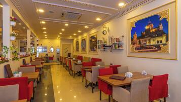 A hotel restaurant with a long counter, multiple tables, and chairs. There are wall-mounted clocks and framed pictures.