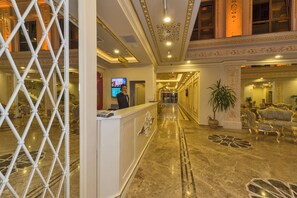 A hotel lobby with a reception desk, a TV screen, a staircase, and ornate wall decorations. - Harmony Hotel (Istanbul)