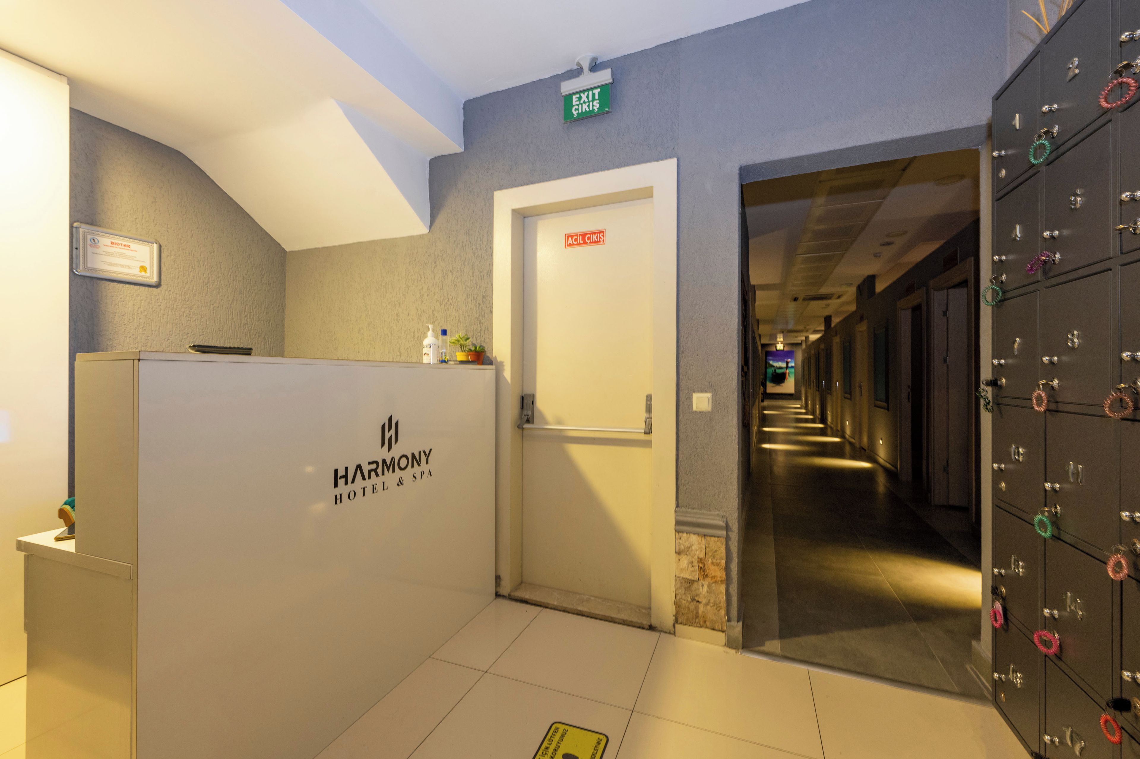 Zona de recepción de hotel con un mostrador, una puerta que indica 'EXIT GIRI' y un pasillo que da a una habitación con vistas.