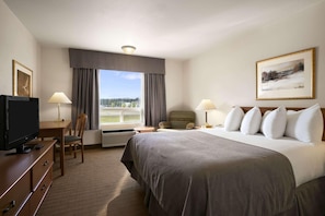 Habitación de hotel con cama, escritorio, televisión y ventana con cortinas.
