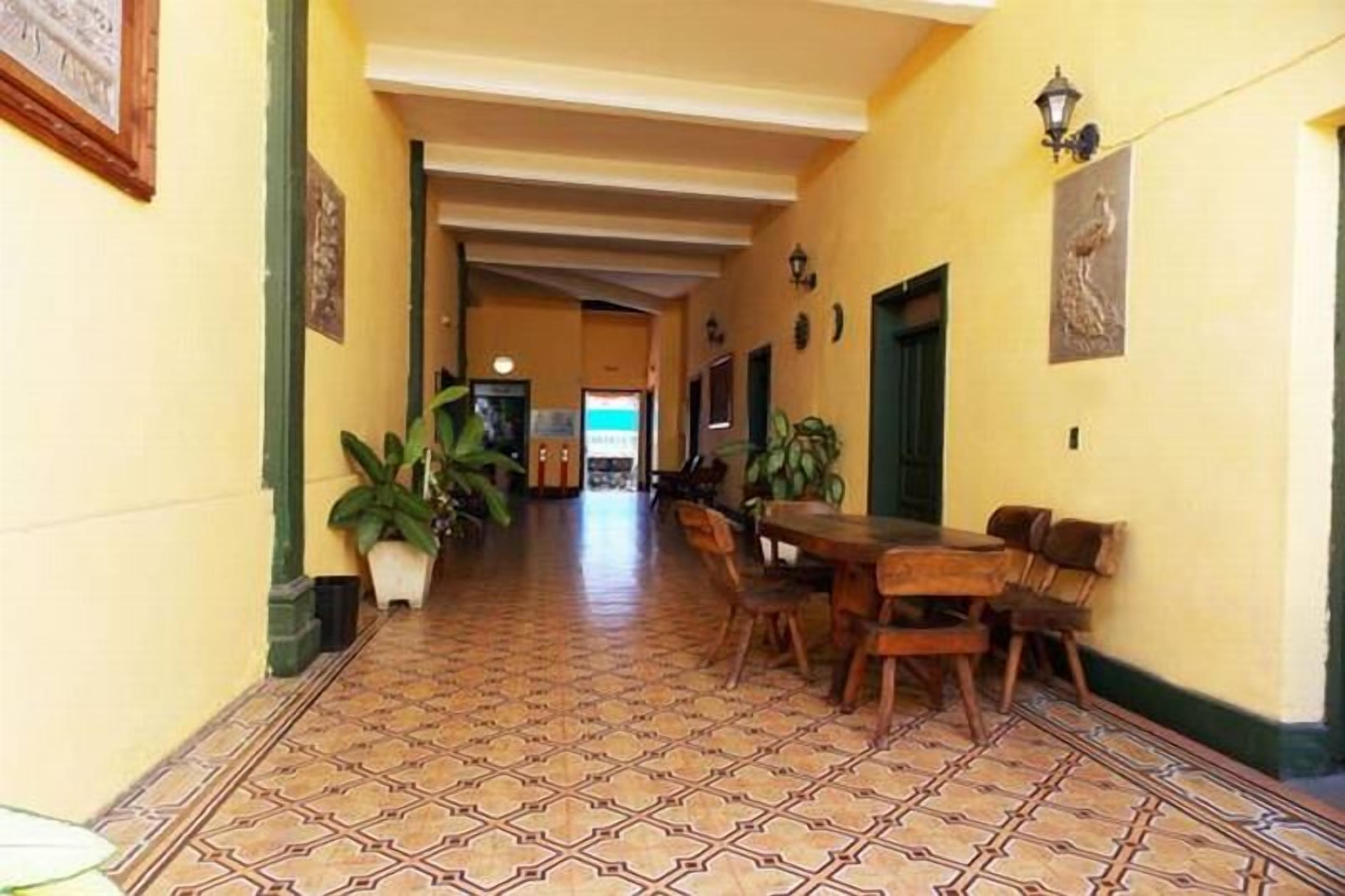 A hallway with patterned floor tiles, a dining area with wooden furniture, and wall-mounted artwork.