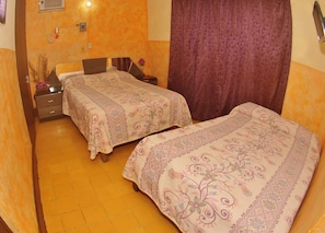 Une chambre avec deux lits, une table de chevet, un vase de fleurs et un rideau.