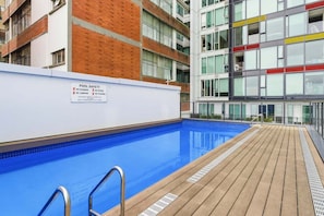 A pool area with a safety sign, a wooden deck, and a modern building with multiple windows. - Stylish Apartment 130m to Int Conference Centre (Auckland CBD)